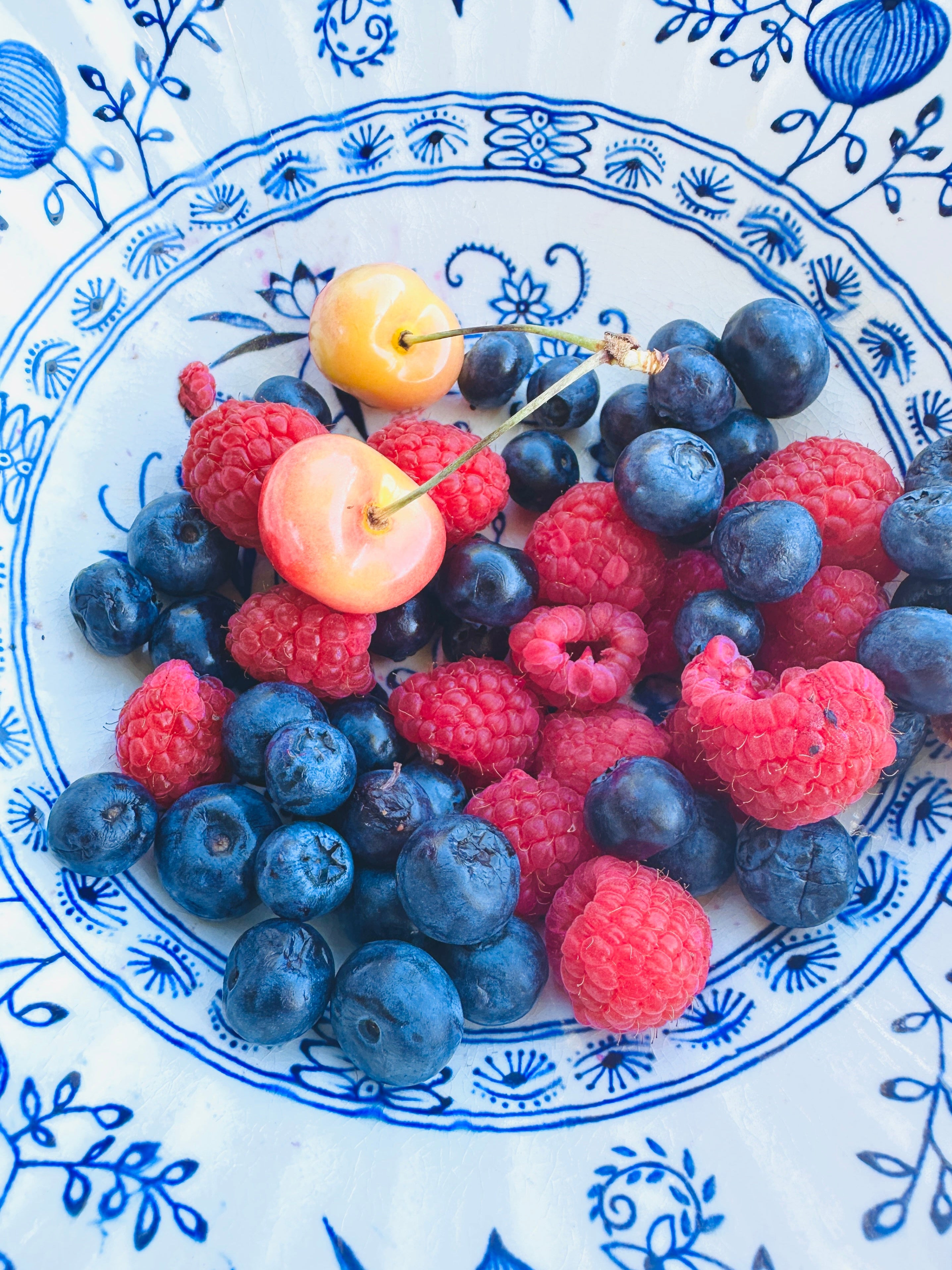 Fruit including blueberries, raspberries, and cherries on a decorative blue and white plate.