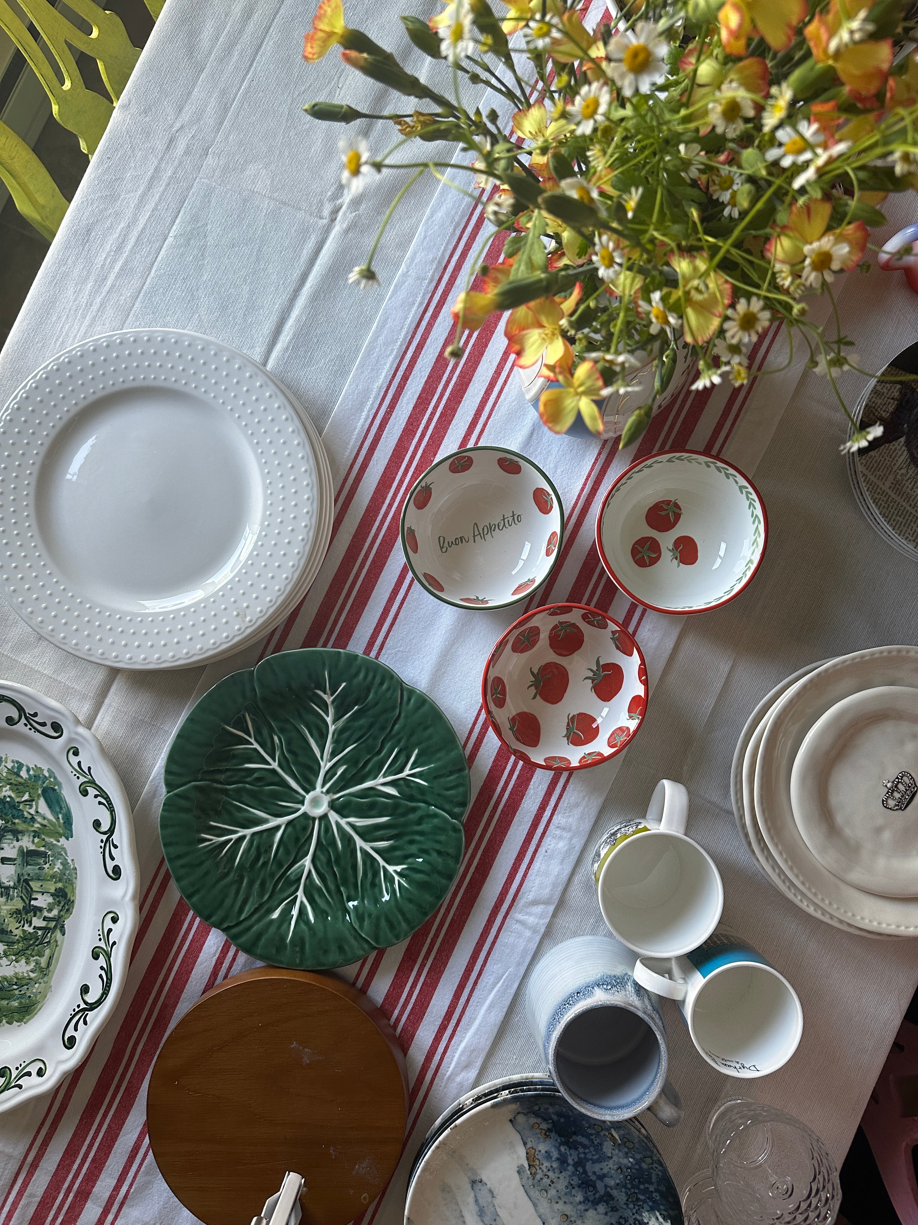 Table setting with various ceramic plates, bowls, and cups on a striped tablecloth.