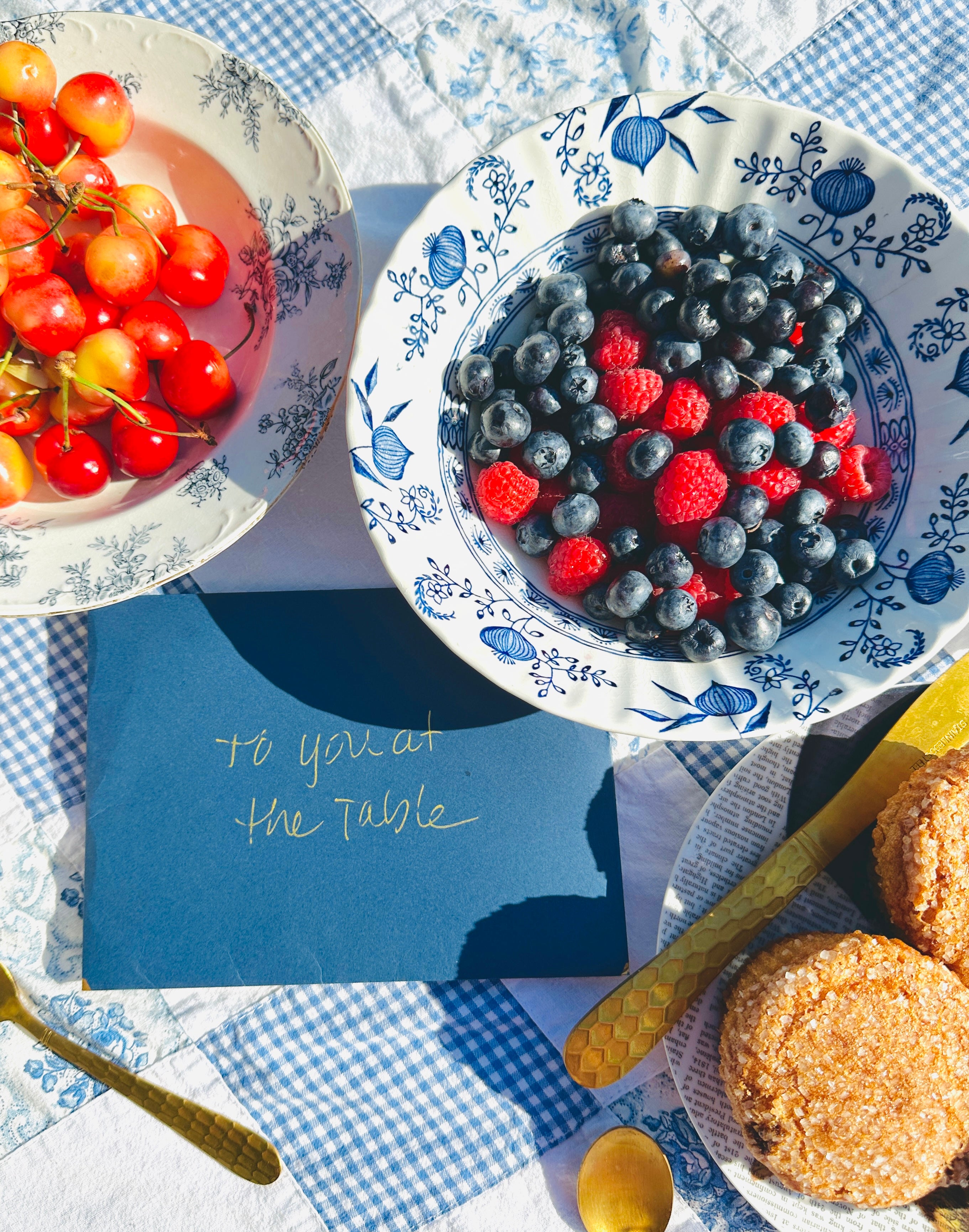 Bowl of berries on a checkered tablecloth with a card and cookies.