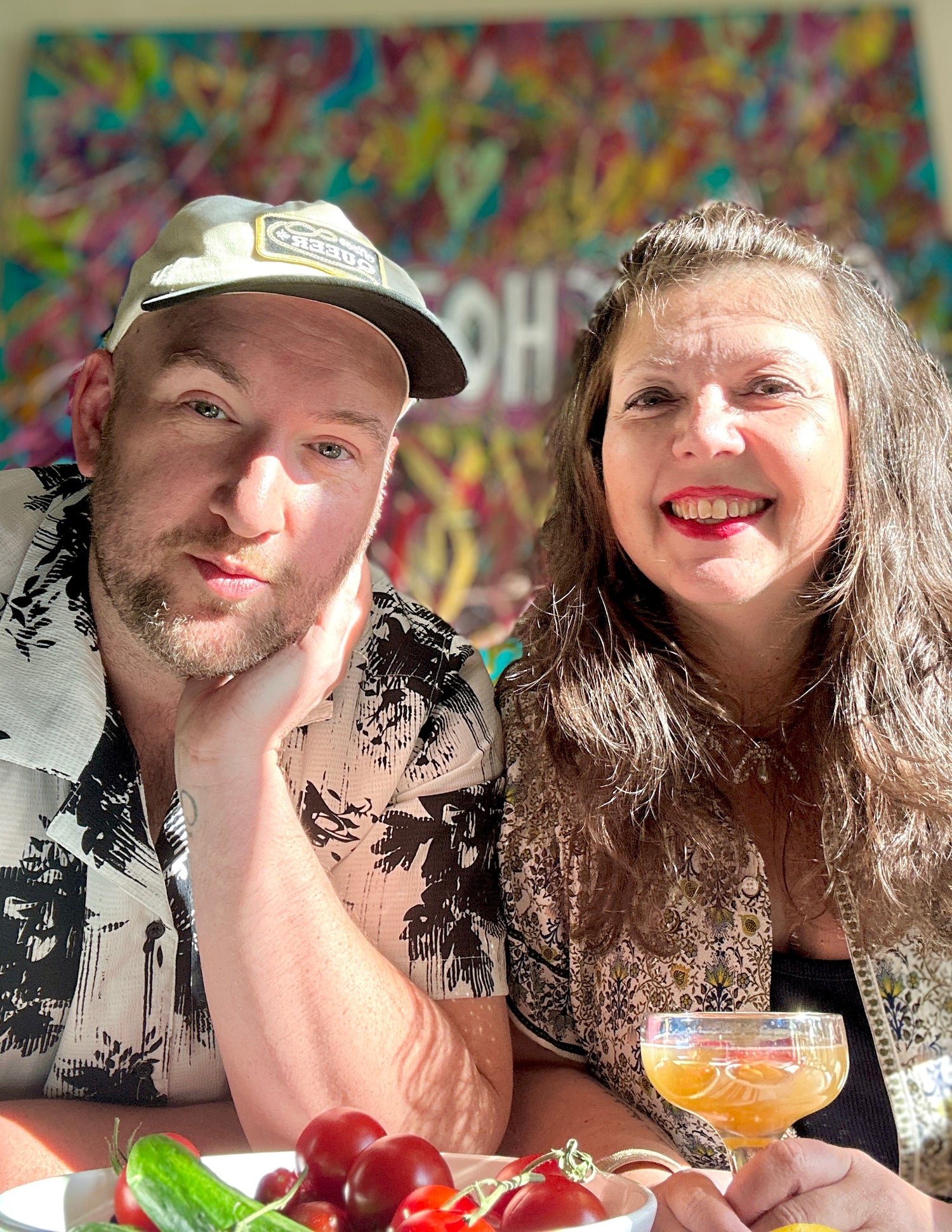 Two people sitting together with a colorful mural in the background