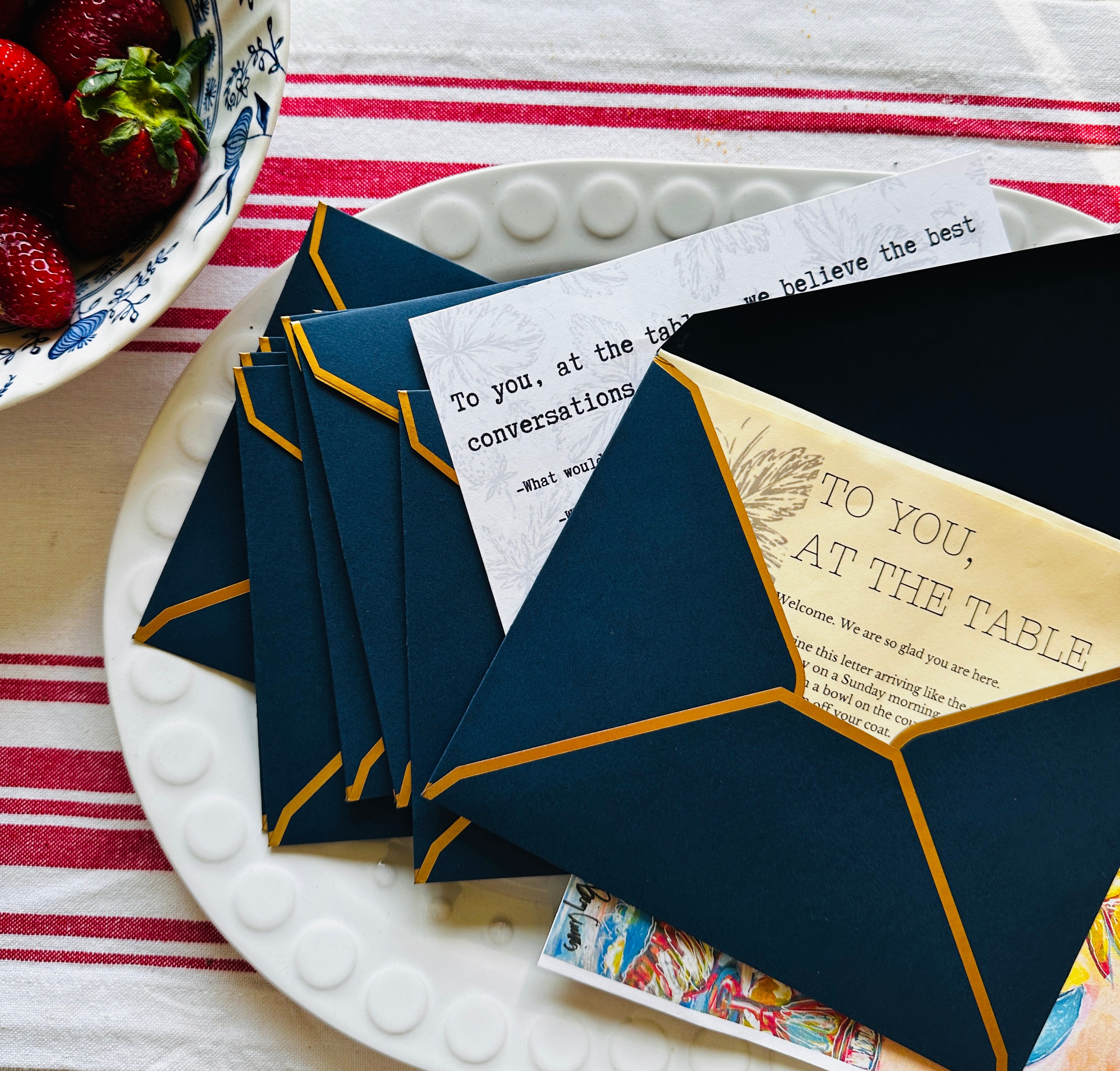 Navy blue envelopes with gold accents on a white plate with strawberries in the background
